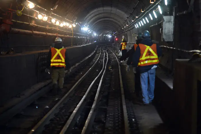 MTA workers wearing reflective vests walk along the subterranean E train subway tracks in NYC.